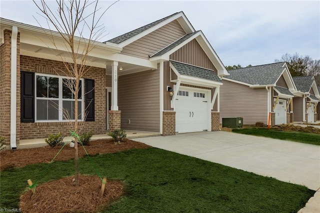 craftsman inspired home with driveway, a front yard, an attached garage, brick siding, and central AC unit