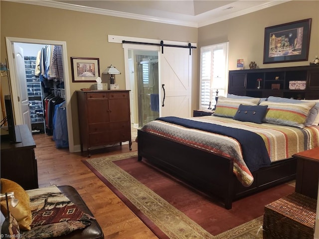 bedroom featuring a walk in closet, ornamental molding, a barn door, and wood-type flooring