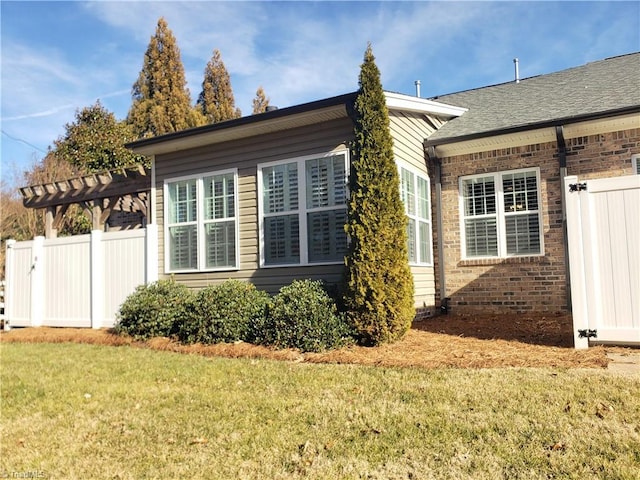 view of property exterior featuring a shingled roof, brick siding, fence, and a lawn