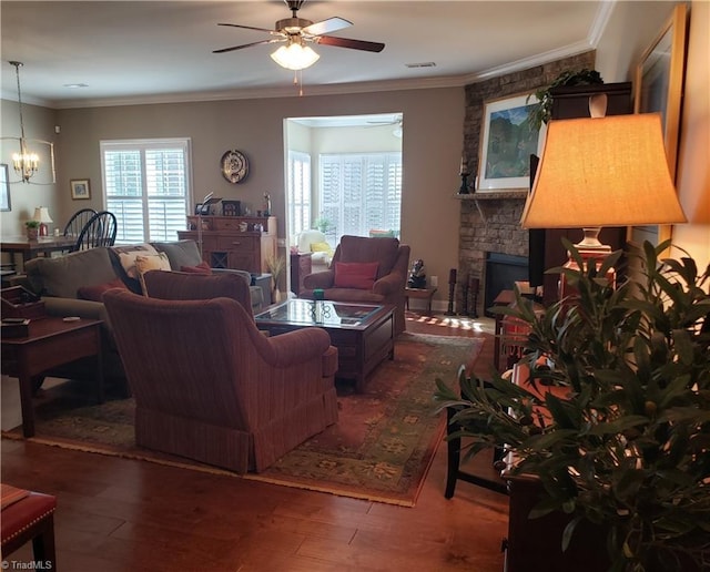 living room with crown molding, a stone fireplace, ceiling fan with notable chandelier, and dark hardwood / wood-style floors