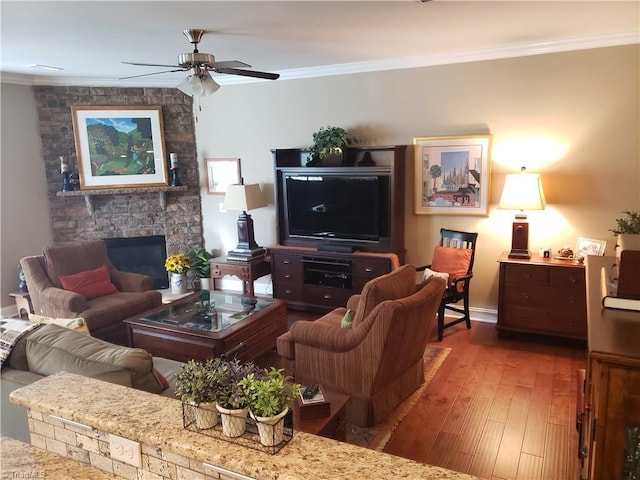 living room featuring crown molding, wood-type flooring, a stone fireplace, and ceiling fan