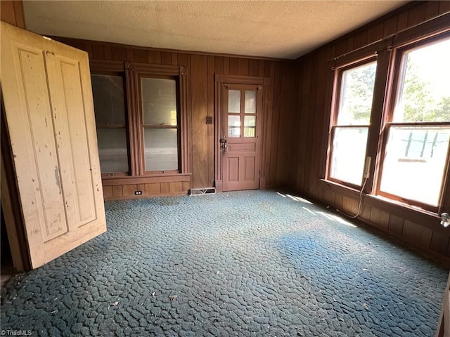 carpeted empty room with wooden walls, a textured ceiling, and visible vents