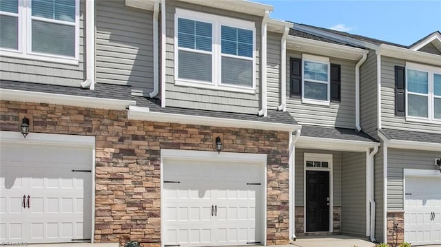 townhome / multi-family property with stone siding, an attached garage, and a shingled roof