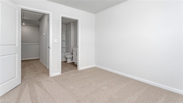 unfurnished bedroom featuring baseboards, carpet floors, attic access, ensuite bath, and a walk in closet