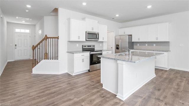 kitchen with light wood-style flooring, a center island with sink, a sink, appliances with stainless steel finishes, and white cabinets