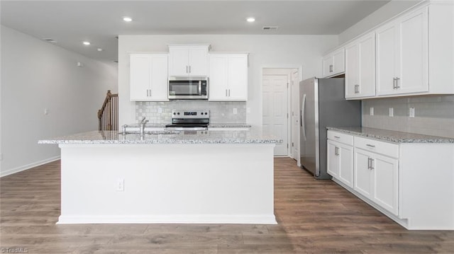 kitchen featuring wood finished floors, a center island with sink, a sink, white cabinets, and appliances with stainless steel finishes