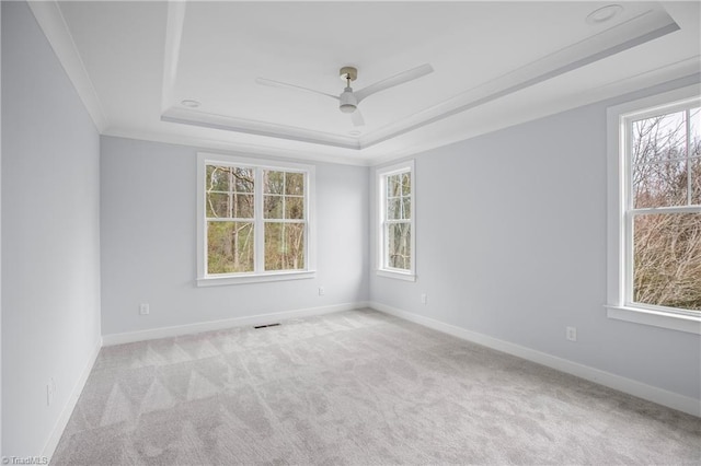 empty room with visible vents, light carpet, baseboards, a tray ceiling, and a ceiling fan