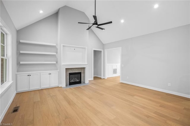 unfurnished living room with ceiling fan, visible vents, a fireplace, high vaulted ceiling, and light wood-style flooring