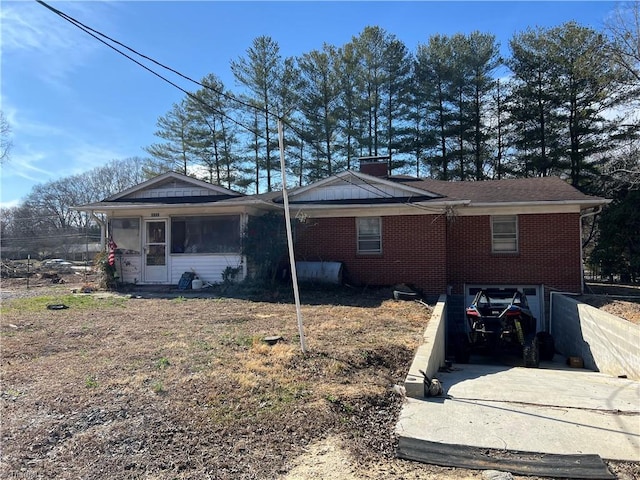 view of side of home with driveway, a garage, a sunroom, a chimney, and brick siding