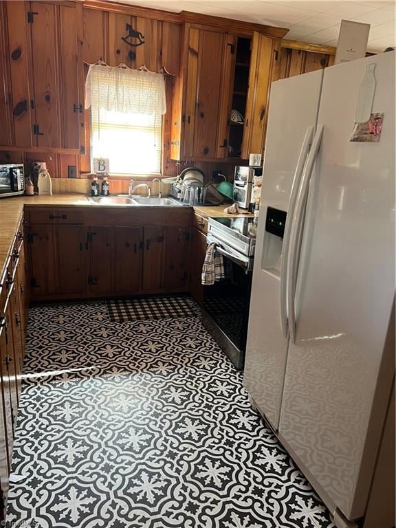 kitchen with brown cabinetry, glass insert cabinets, appliances with stainless steel finishes, light countertops, and a sink