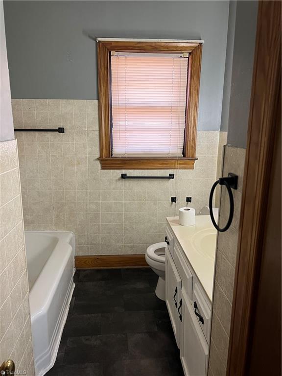 full bath featuring toilet, a wainscoted wall, a washtub, vanity, and tile walls