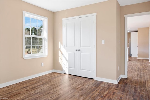 unfurnished bedroom featuring a closet, dark wood-type flooring, and baseboards