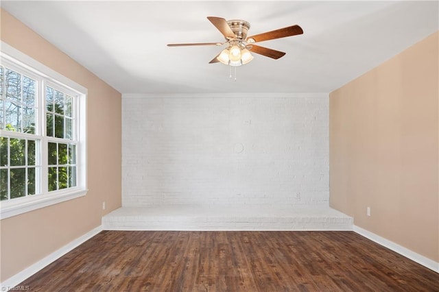 empty room with ceiling fan, baseboards, dark wood-type flooring, and brick wall