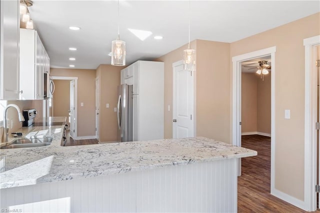 kitchen with light stone countertops, dark wood-style flooring, freestanding refrigerator, a sink, and white cabinets