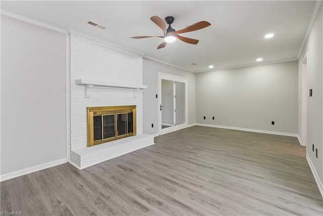 unfurnished living room featuring wood-type flooring, ornamental molding, ceiling fan, and a brick fireplace