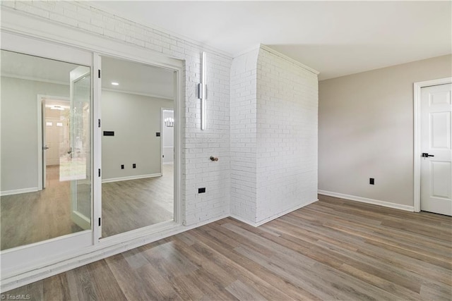 empty room with wood-type flooring, brick wall, and crown molding