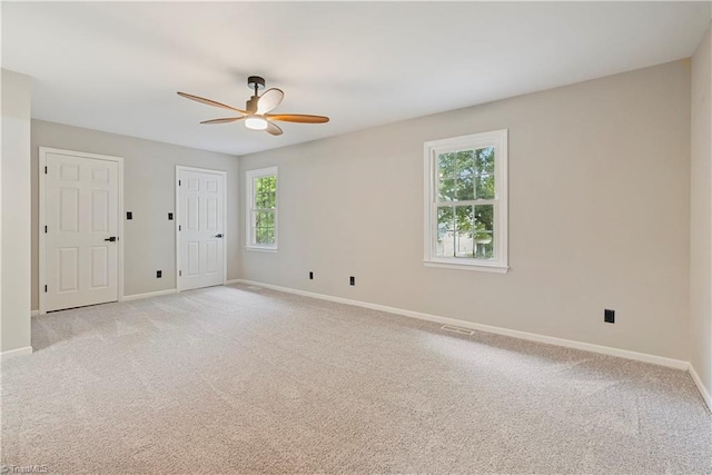 spare room with ceiling fan, light colored carpet, and plenty of natural light