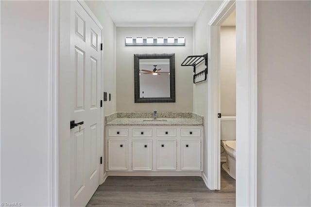 bathroom with wood-type flooring, vanity, toilet, and ceiling fan