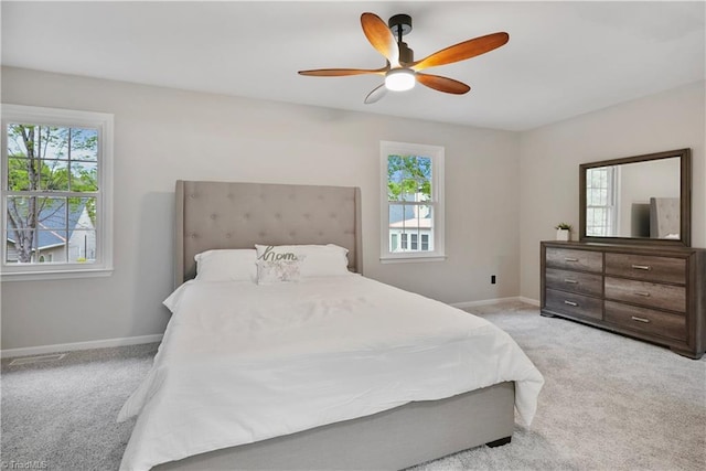 bedroom featuring a ceiling fan, multiple windows, light colored carpet, and baseboards