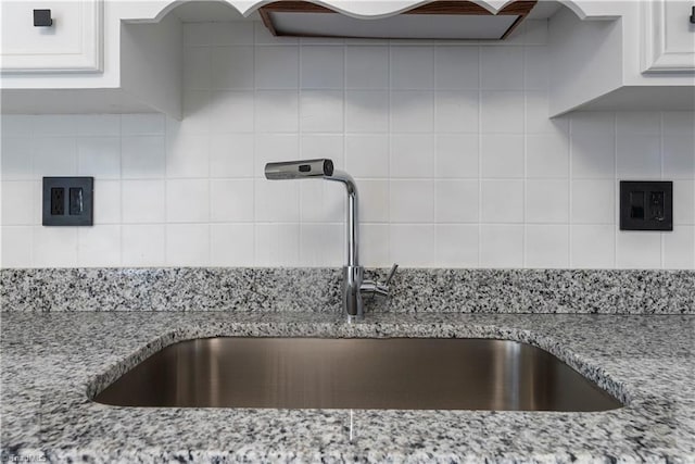 room details featuring white cabinets, light stone counters, tasteful backsplash, and sink