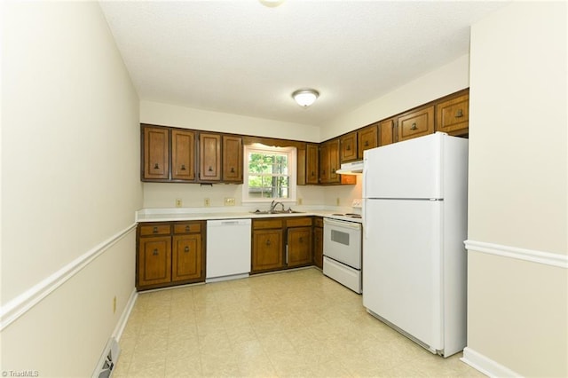 kitchen with white appliances, a sink, under cabinet range hood, light countertops, and brown cabinets