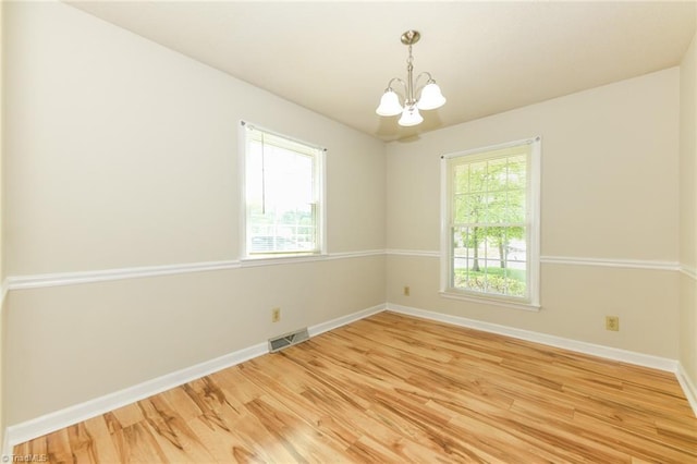 spare room with a chandelier, light wood-style floors, and baseboards