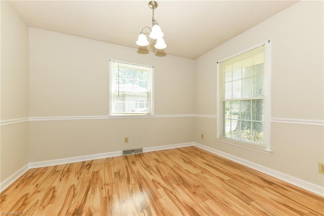 empty room featuring a chandelier, light wood-style flooring, and baseboards