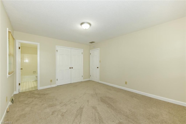 unfurnished bedroom featuring light carpet, baseboards, a closet, and ensuite bathroom