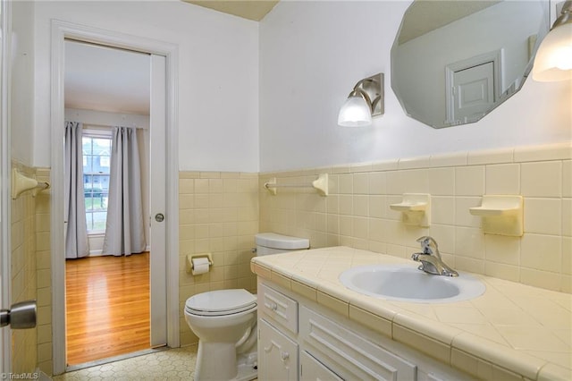 bathroom featuring toilet, tile walls, wainscoting, and vanity