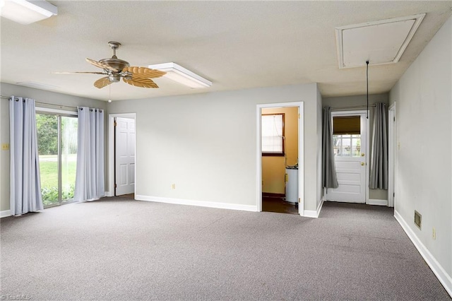 carpeted empty room featuring attic access, a ceiling fan, and baseboards