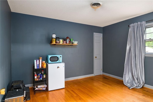 interior space with baseboards, visible vents, refrigerator, and wood finished floors