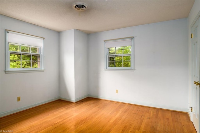 spare room featuring light wood finished floors, visible vents, and baseboards