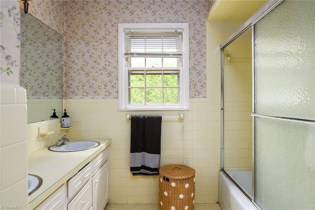 bathroom featuring tile walls, wallpapered walls, a wainscoted wall, and a sink