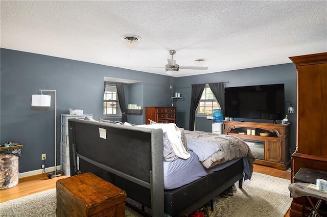 bedroom with a textured ceiling, multiple windows, wood finished floors, and visible vents