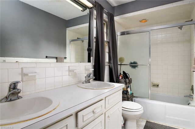 full bathroom featuring toilet, double vanity, a sink, and shower / bath combination with glass door