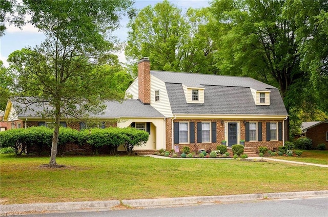 dutch colonial with a front yard, a gambrel roof, a shingled roof, brick siding, and a chimney
