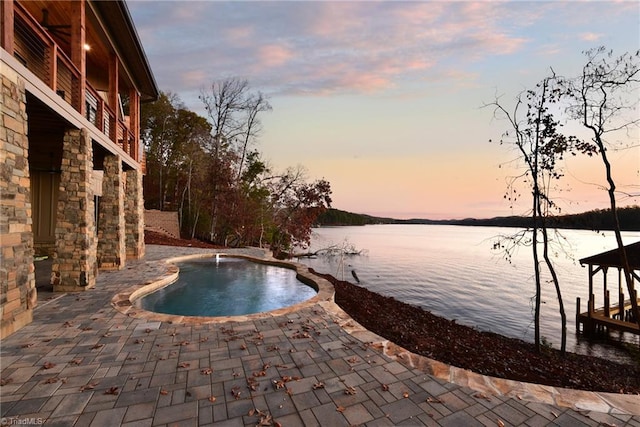 pool at dusk featuring a patio area and a water view