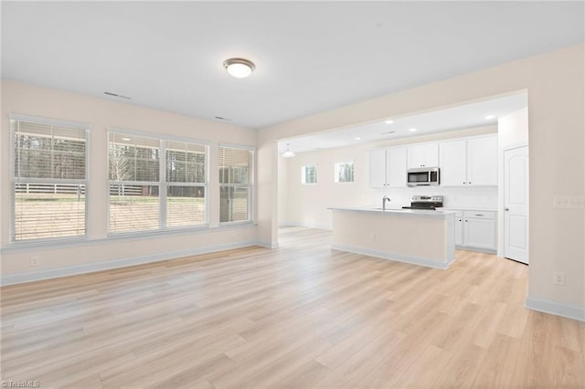 kitchen with sink, white cabinetry, appliances with stainless steel finishes, a kitchen island with sink, and light hardwood / wood-style floors