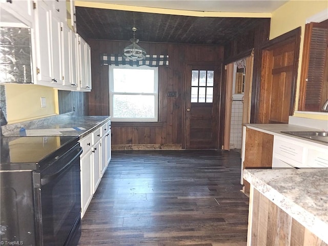 kitchen featuring wood walls, black electric range oven, white cabinetry, and hanging light fixtures