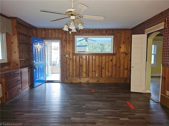 interior space featuring ceiling fan, dark wood-type flooring, and wood walls