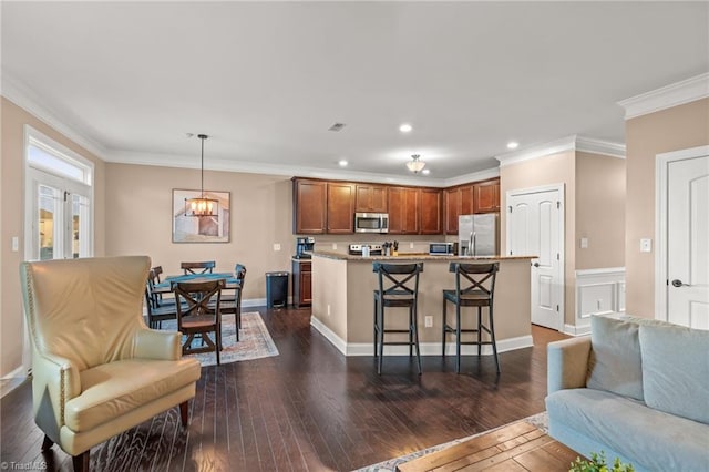 kitchen featuring dark wood-type flooring, pendant lighting, a breakfast bar area, appliances with stainless steel finishes, and ornamental molding