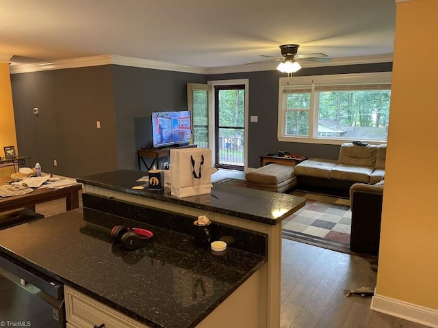 kitchen featuring wood-type flooring, dark stone counters, ceiling fan, a kitchen island, and ornamental molding