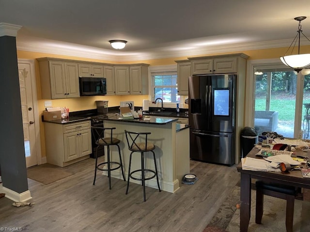 kitchen featuring decorative light fixtures, black appliances, wood-type flooring, sink, and a breakfast bar area