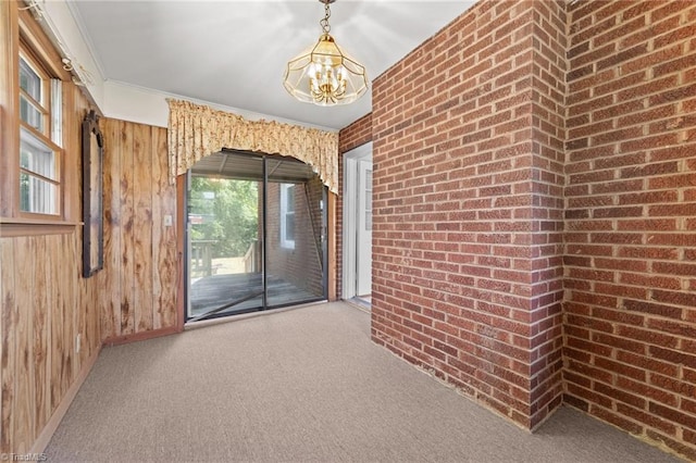 spare room featuring crown molding, carpet flooring, an inviting chandelier, brick wall, and wood walls