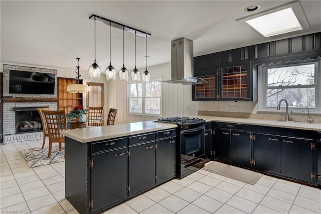 kitchen with black stove, hanging light fixtures, island range hood, a fireplace, and light tile patterned floors