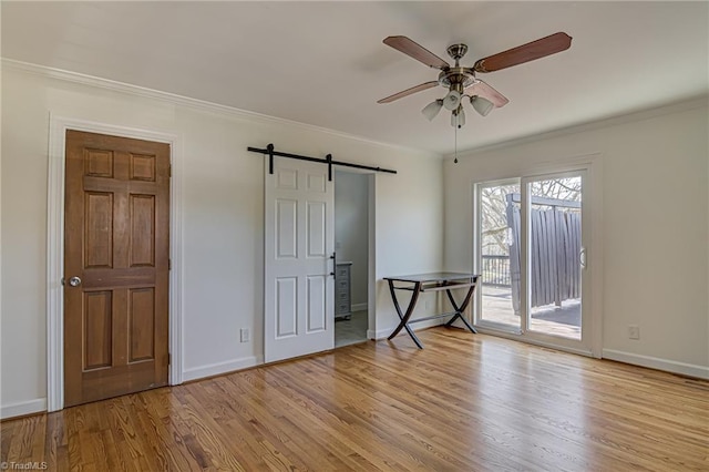 unfurnished bedroom featuring access to outside, crown molding, light hardwood / wood-style flooring, ceiling fan, and a barn door