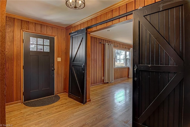 entrance foyer with a barn door, wooden walls, light hardwood / wood-style flooring, and ornamental molding