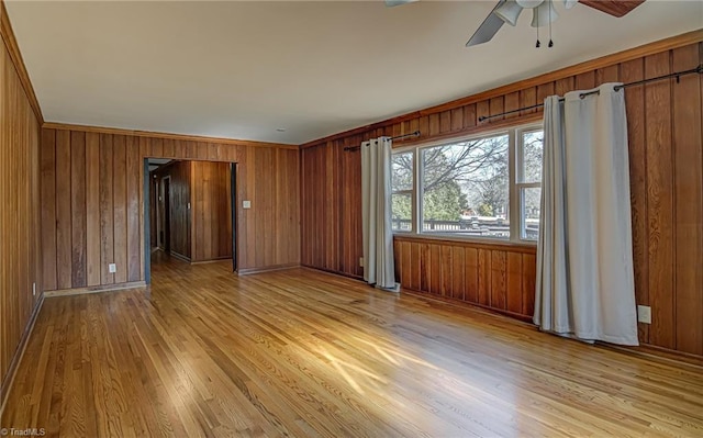 empty room featuring wood walls, ceiling fan, and light wood-type flooring