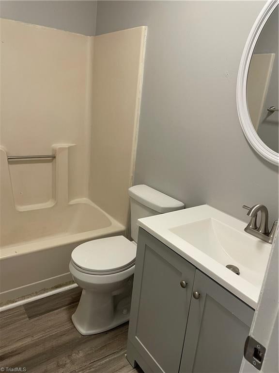 full bathroom featuring wood-type flooring, bathing tub / shower combination, vanity, and toilet