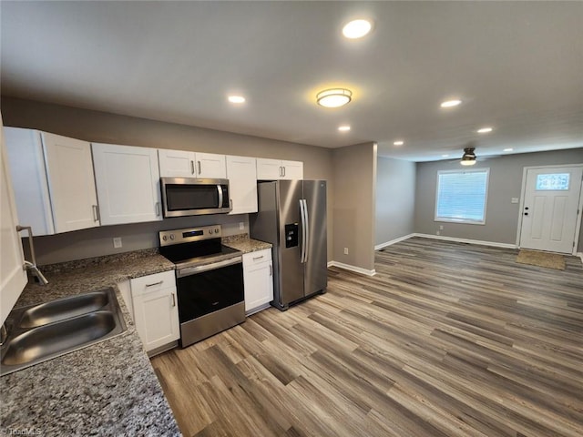 kitchen with sink, white cabinetry, dark stone countertops, hardwood / wood-style flooring, and stainless steel appliances